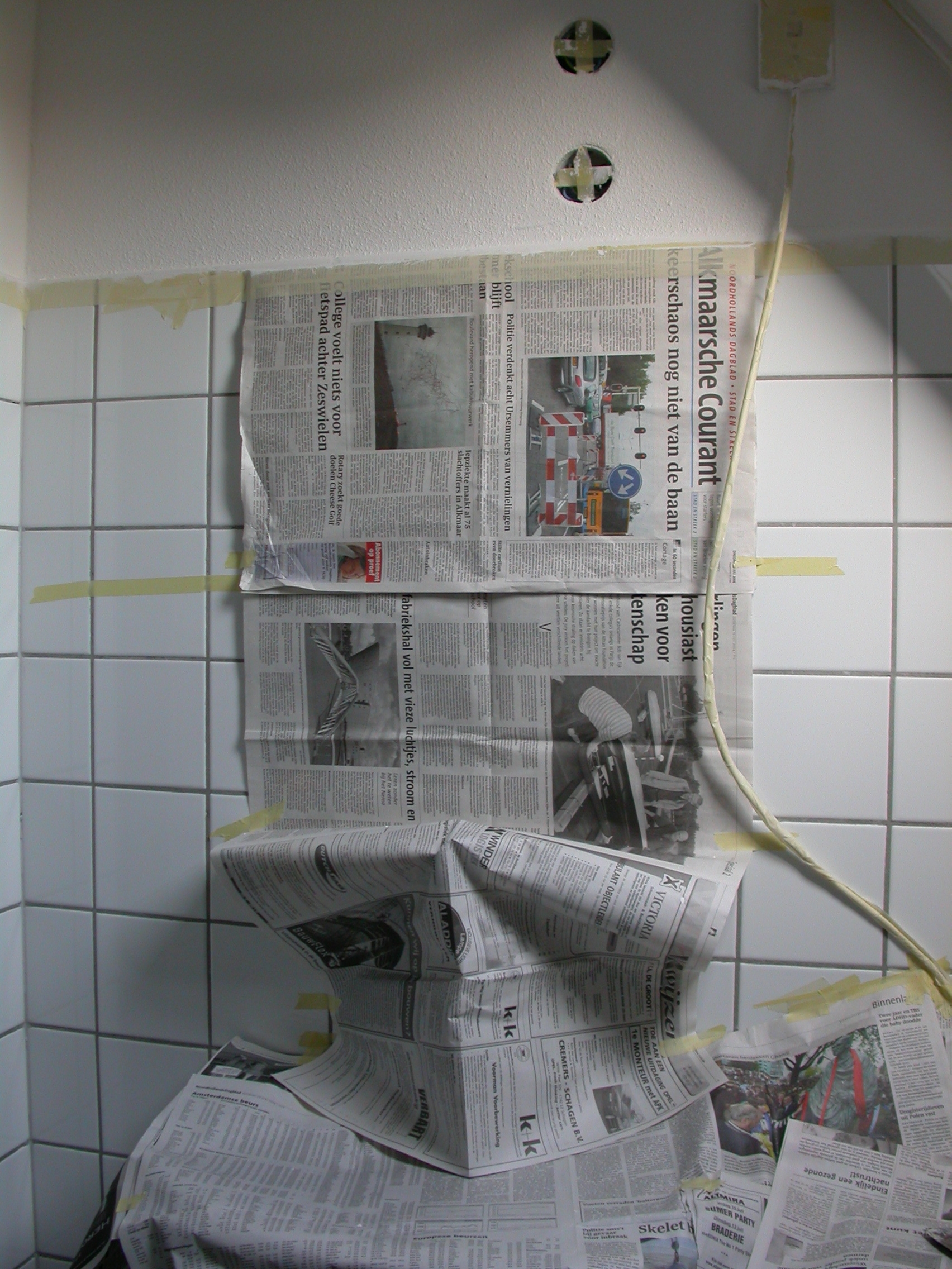 paul sink covered with newspapers taped to a bathroom wall